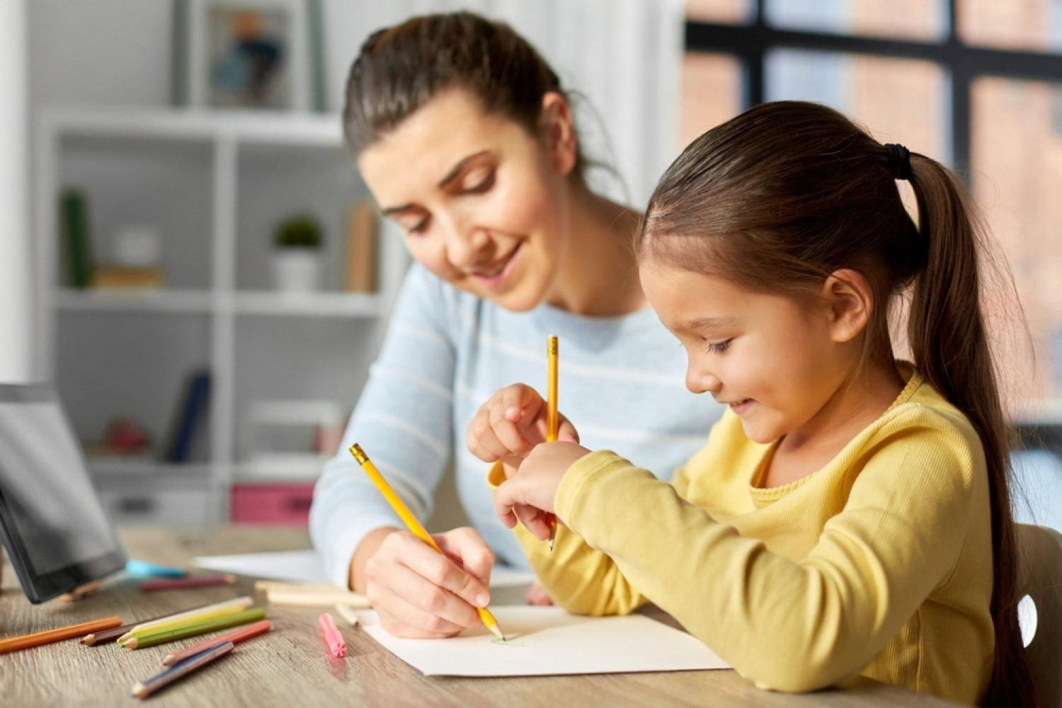 Mother and daughter drawing together with pencils at a bright home desk